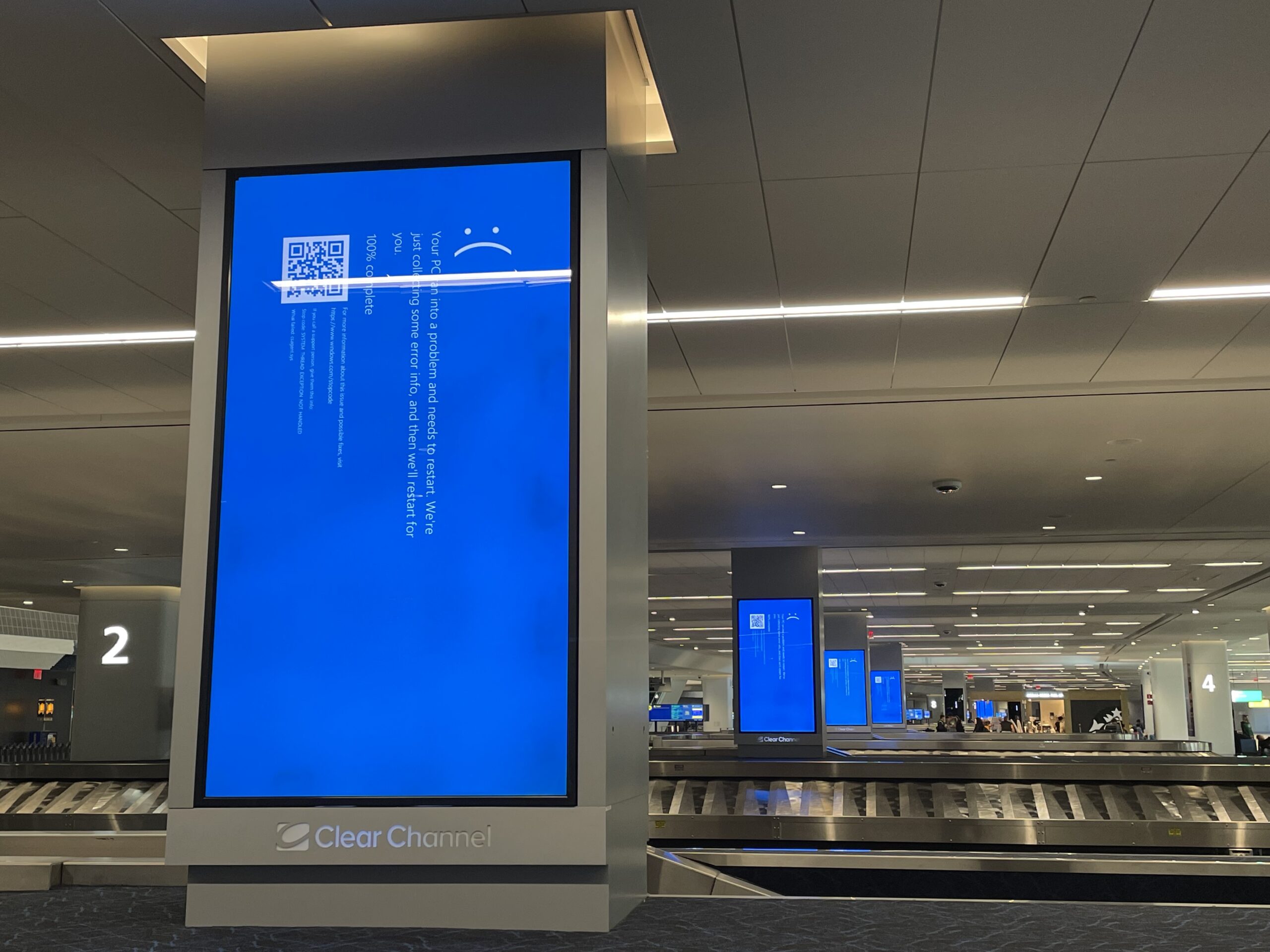 Eine Gepäckhalle in einem Flughafen mit grossen Informationsbildschirmen (hochkant) auf denen um 90 Grad gedreht der BlueScreen von CrowdStrike steht