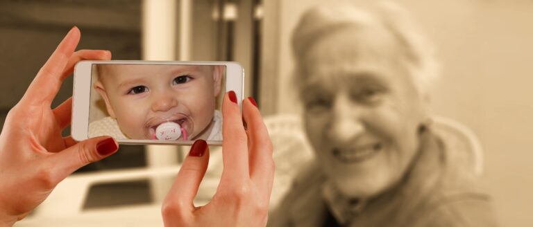 Grossmutter wird mit Handy fotografiert. Dabei zeigt die Photo-App das Bild eines Babies