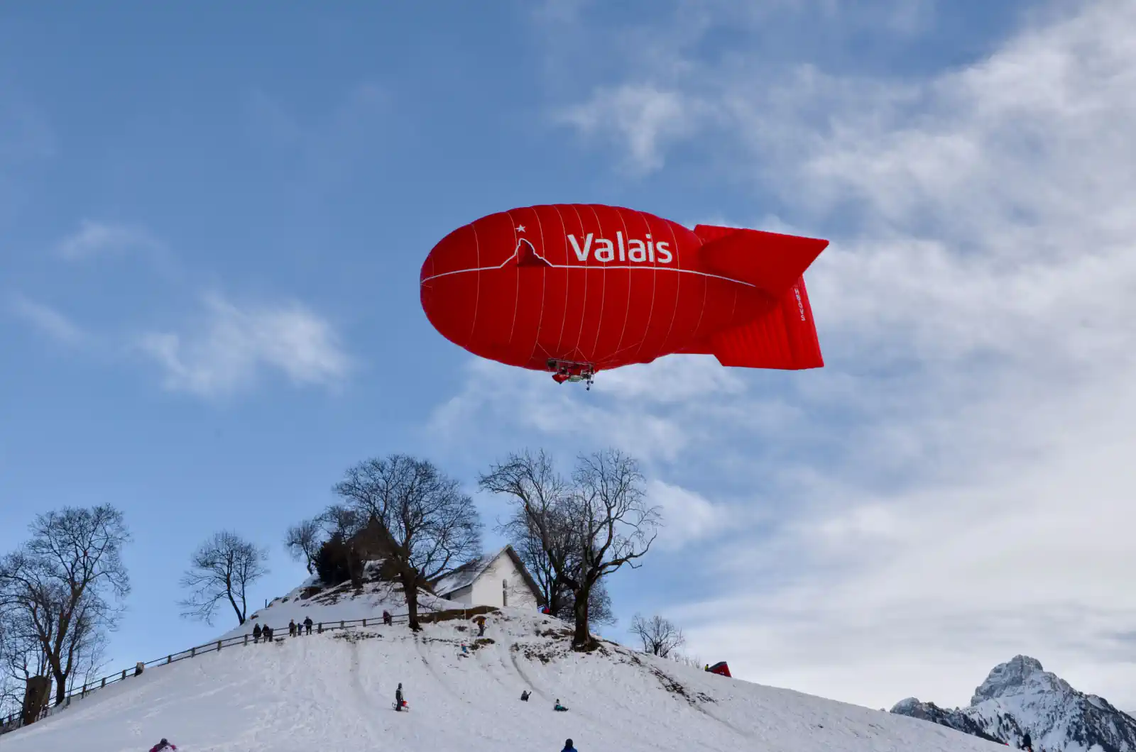 Ein roter Zeppelin vor Wolken über einem Hügel